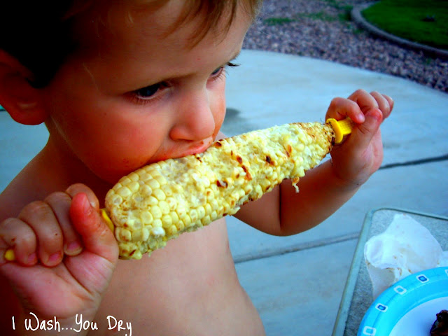 A child taking a bite of grilled corn on the cob. 