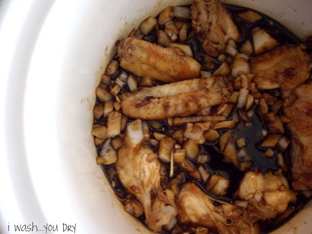 A crockpot of brown sauce, onions and chicken wings. 