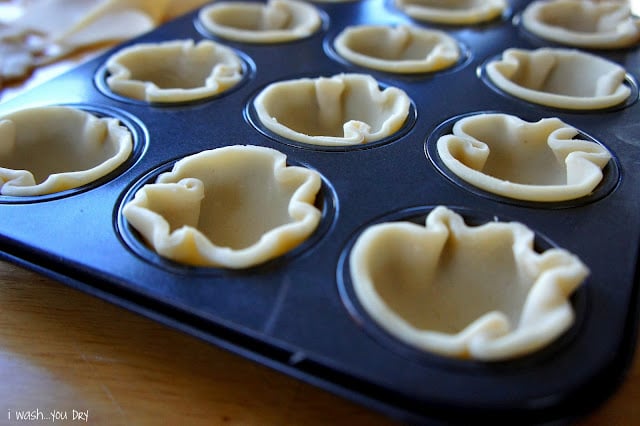 A close up of a muffin tin with each spot lined with pie crust.