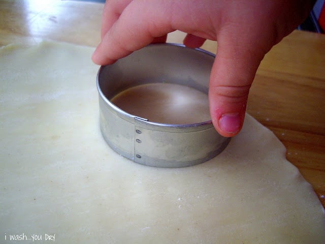 A hand cutting a circle of dough with a round cookie cutter. 