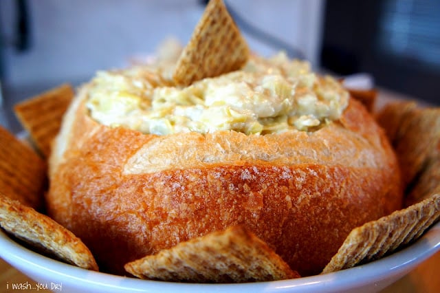 A close up of a round loaf of bread filled with dip and a chip in it on top.