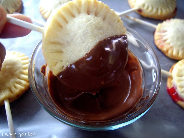 A close up of a mini pie pop being half way dipped into a bowl of melted chocolate.