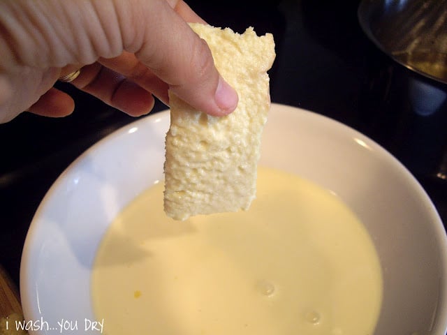 A hand holding a slice of dipped bread over the white liquid. 