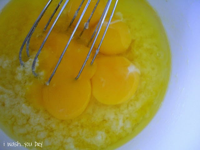 A wire whisk stirring four eggs into the mixture in a bowl. 