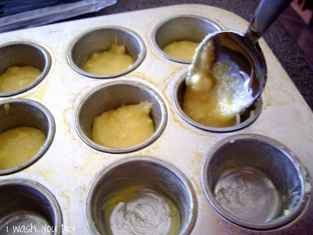 A greased muffin tin with a spoon adding a little muffin mix to each spot. 