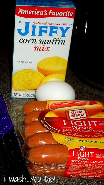 A display of needed ingredients, corn muffin mix, 1 egg and a package of hotdogs. 