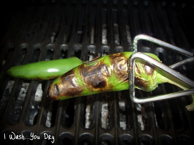Tongs turning jalapeños on a grill.