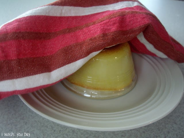 A plate with an upside down glass desert cup on it with a dish towel on top. 