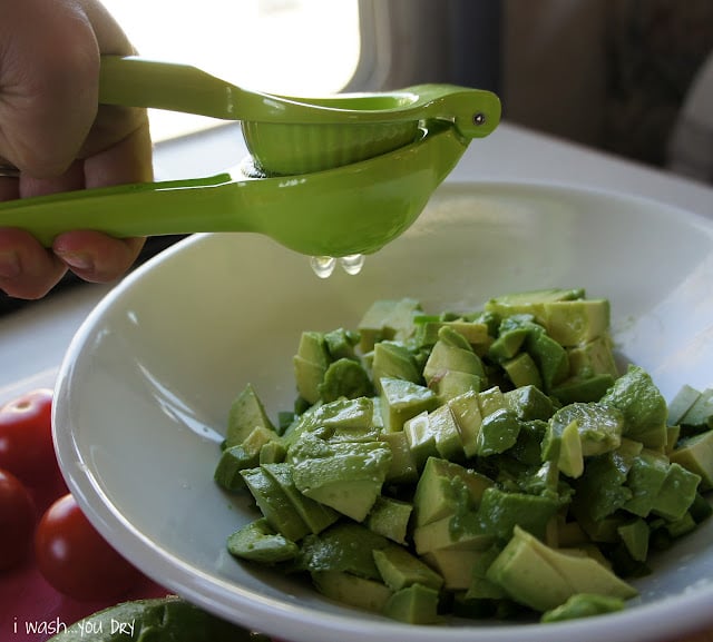 A hand squeezing lime juice over chopped avocado in a bowl.