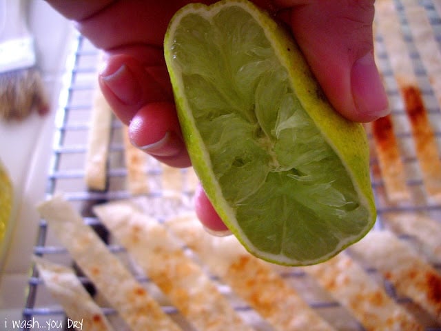 A hand squeezing lime juice onto strips of tortilla.