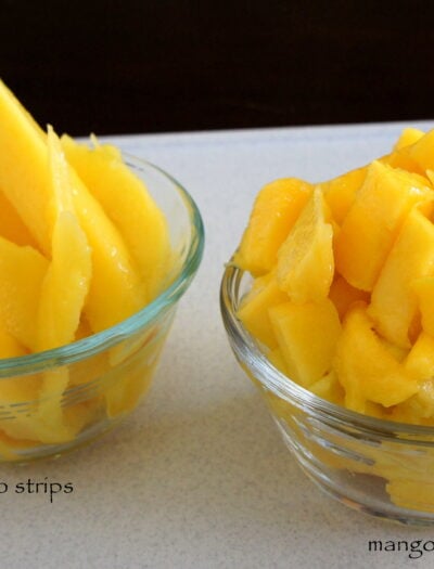 Two small bowls on a table, one with sliced mango and one with cubed mango in them