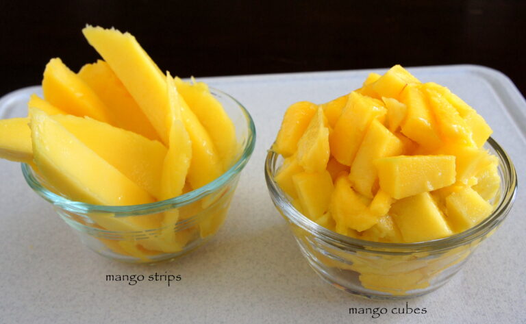 Two small bowls on a table, one with sliced mango and one with cubed mango in them