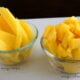 Two small bowls on a table, one with sliced mango and one with cubed mango in them