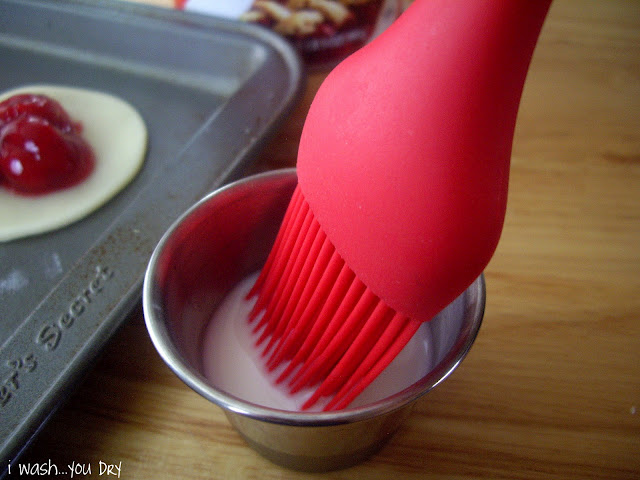 A pastry brush dipped into a small cup of milk.