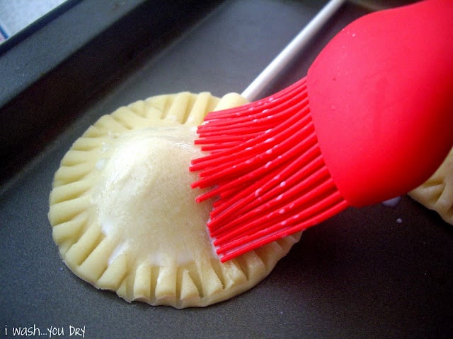 A pastry brush coating the top layer of the pie crust with milk.