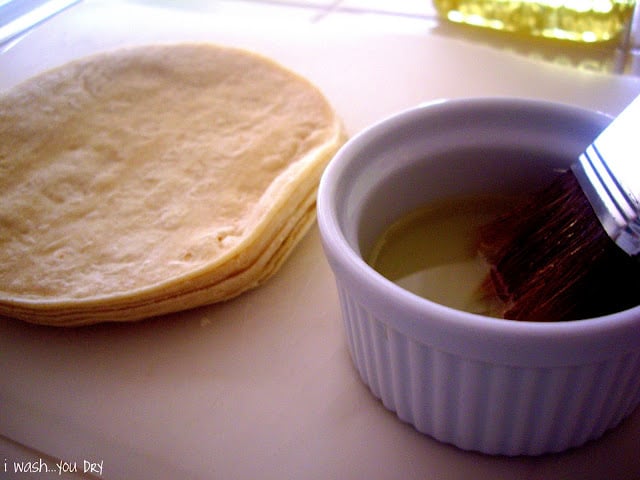 A stack of small tortillas next to a bowl of oil.