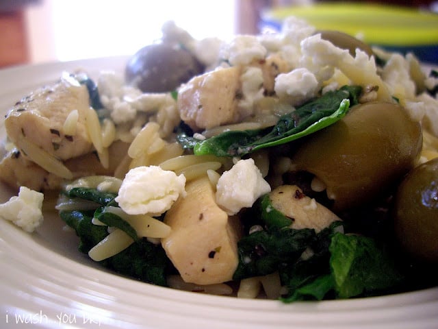 A close up of food in a bowl, chicken, olives, spinach and cheese.