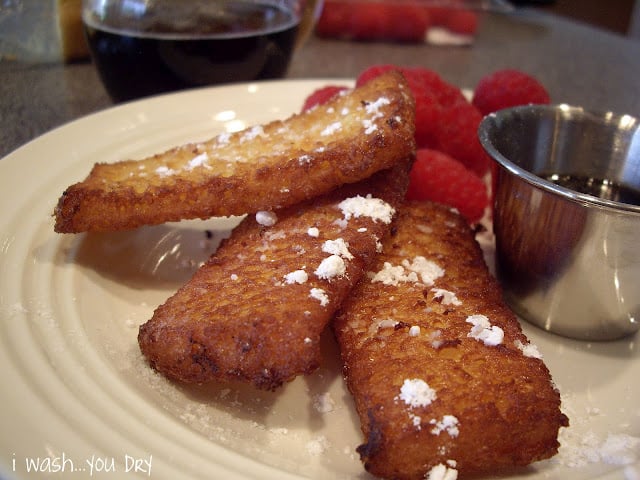 A display of french toast strips sprinkled with powdered sugar with a side of raspberries. 