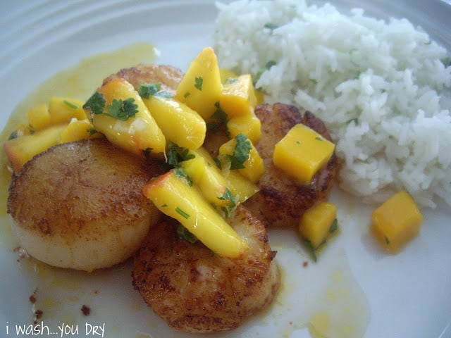 A plate displaying fried scallops topped with mango and peach salsa next to a side of rice. 