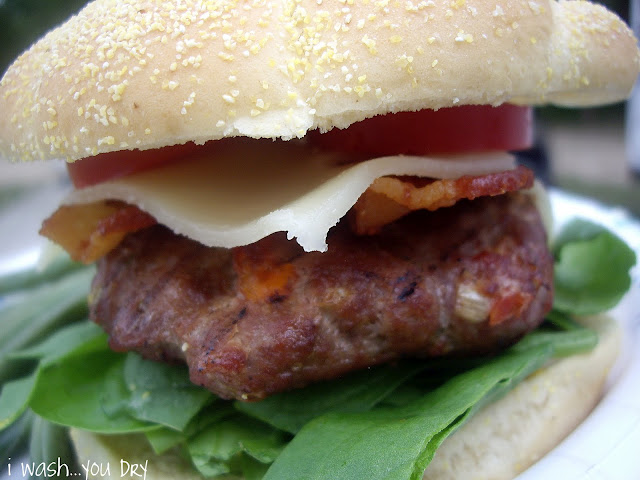 A close up of a burger, cheese, bacon, a tomato slice, and lettuce between two buns.