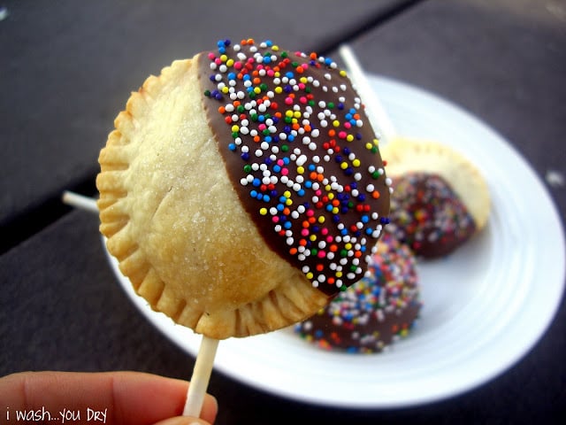 A hand holding a mini pie pop partially dipped in chocolate and sprinkles.