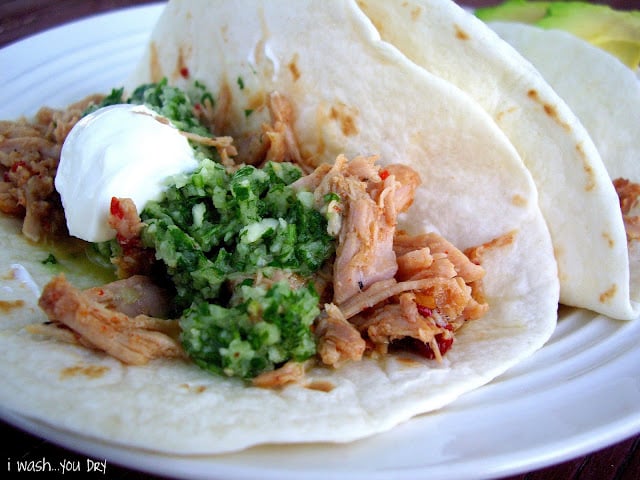 Close up of shredded pulled pork in a flour tortilla topped with veggies and sour cream. 