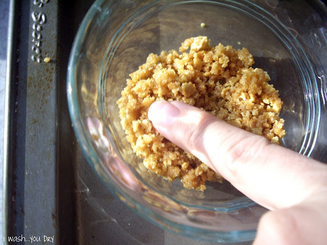 A finger pressing the graham cracker mixture into the bottom of a small glass dish. 