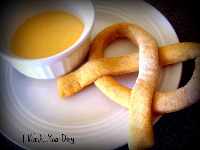 A homemade pretzel on a plate next to a small bowl of dipping sauce. 