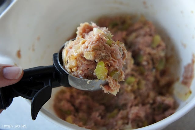 A close up of an ice cream scooper with a scoop of raw meatloaf above the bowl.