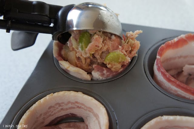 An ice cream scooper adding a scoop of raw meatloaf to a bacon lined muffin tin.