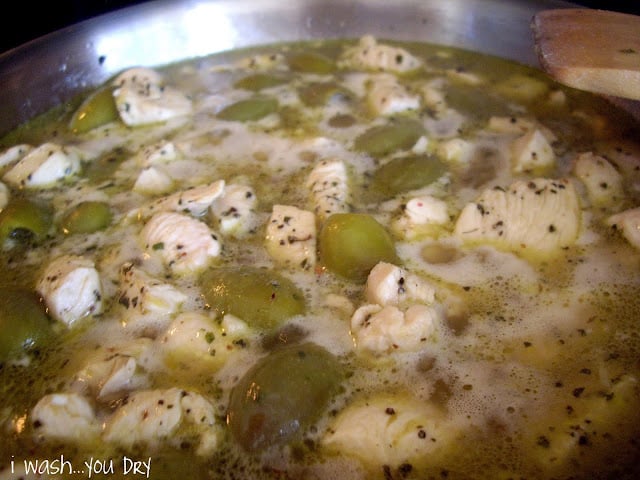 Chicken and olives simmering in a pan. 