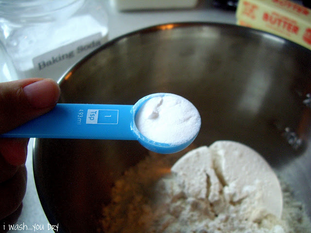 A measuring spoon of baking soda over a mixing bowl with more ingredients in it. 