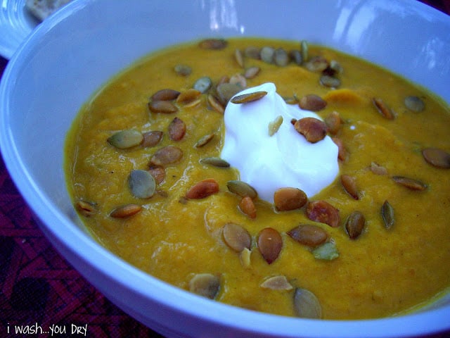 A close up of a bowl of soup topped with pumpkin seeds and sour cream. 