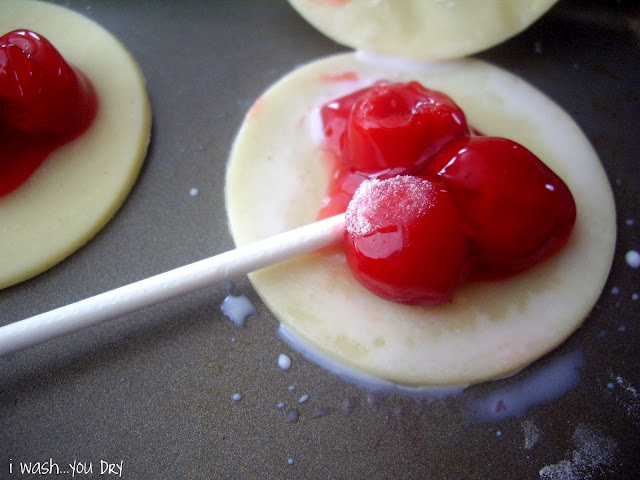 A circle of pie crust topped with three cherries and a sucker stick on a baking pan. 