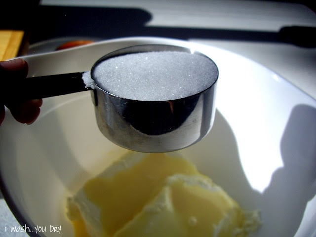 A measuring cup of sugar above a mixing bowl. 