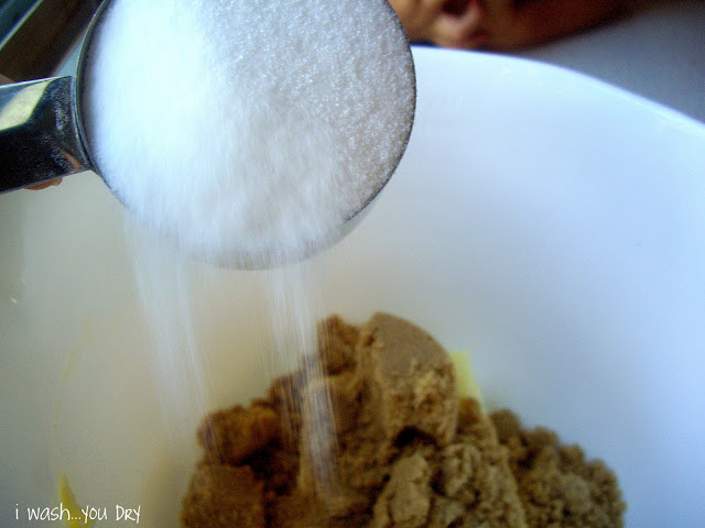 A measuring cup of sugar being added to a bowl of ingredients. 