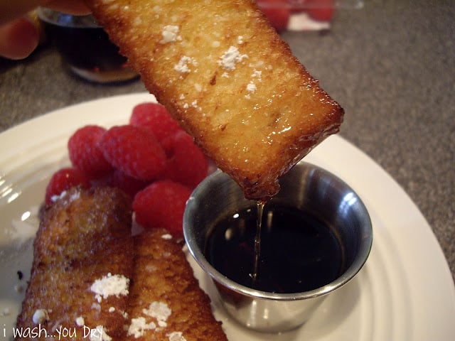 A French toast strip being dipped into a small cup of syrup. 