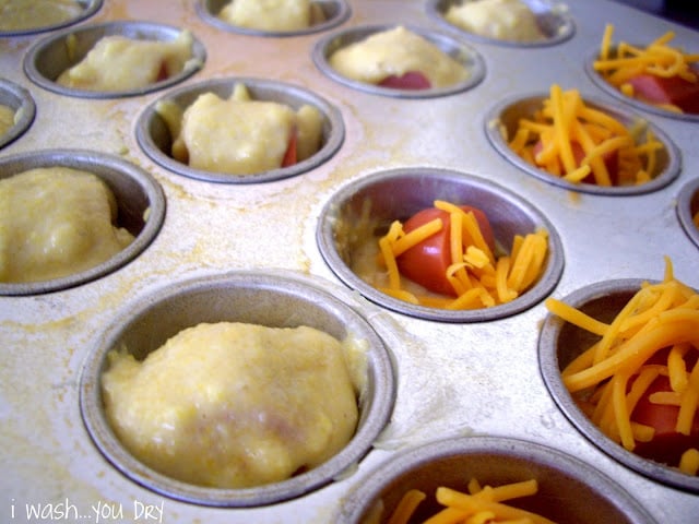 A muffin tin with shredded cheese added on top of the hot dog and then topped with muffin mix. 