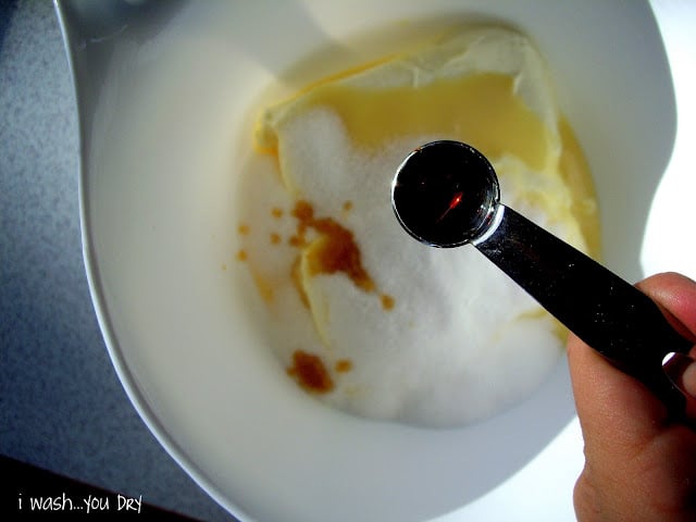 A measuring spoon of vanilla over a mixing bowl with ingredients into it. 