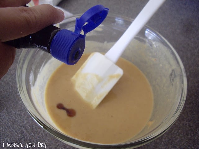 A hand adding vanilla to liquid in a glass bowl. 