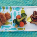 A plate of Cornbread Chicken Nuggets with a side of broccoli and carrots and potato fries