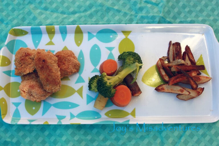 A plate of Cornbread Chicken Nuggets with a side of broccoli and carrots and potato fries