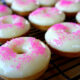 Pink sprinkled glazed donuts on a cooling rack