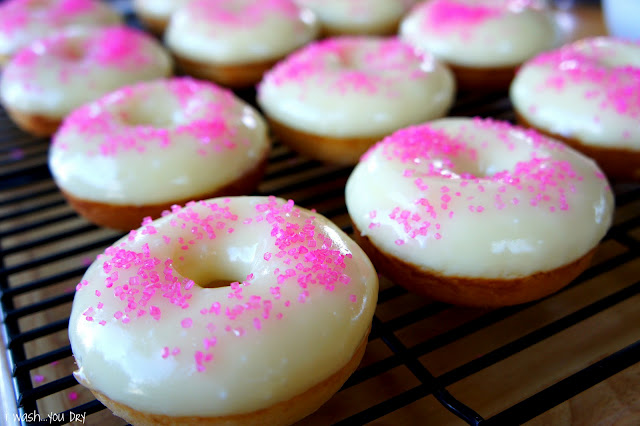 Pink sprinkled glazed donuts on a cooling rack