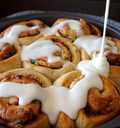 Icing being drizzled on top of a pan of cinnamon rolls
