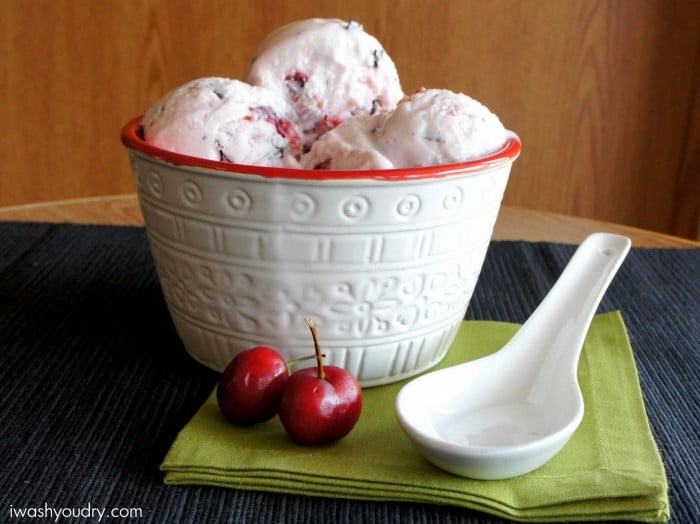 A large bowl filled with scoops of frozen yogurt on a table next to a couple of cherries
