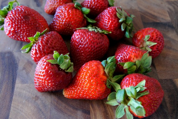 A close up of a pile of fresh strawberries on a cutting board