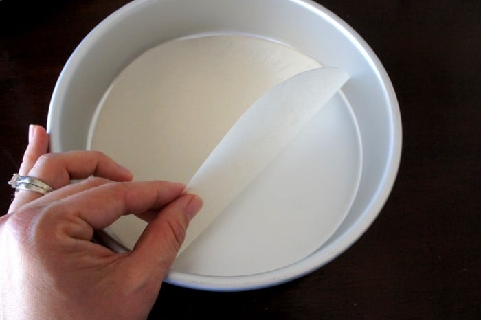 A close up of a round cake pan with a circle of parchment paper being placed on the bottom.
