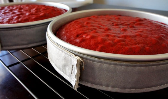 A close up of a metal cake pan cooling on a cooling rack, with red cake