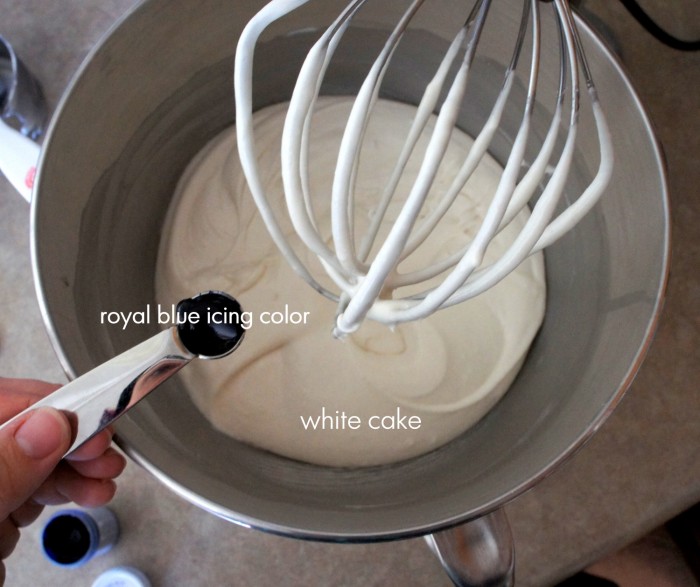 A close up of a mixing bowl with a beater above it and a measuring spoon of vanilla being poured in it